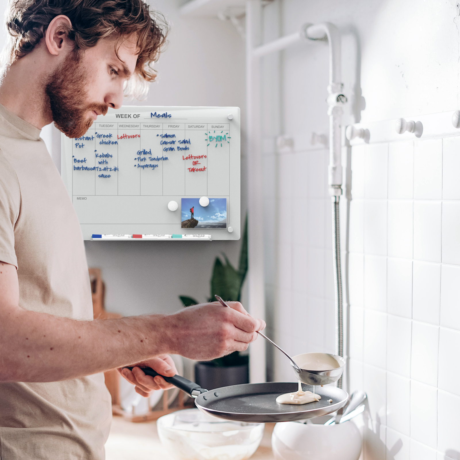 Wall mounted weekly planner in a kitchen behind a man cooking. 