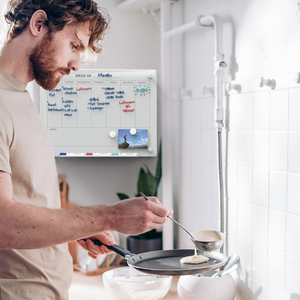 Wall mounted weekly planner in a kitchen behind a man cooking. 