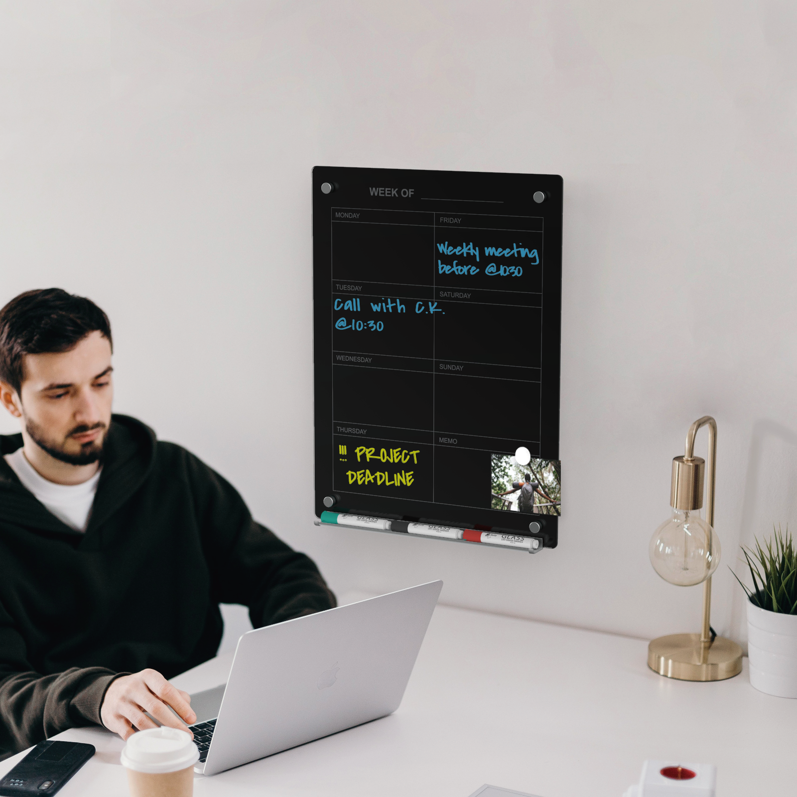 Black glass weekly planner wall mounted next to a person working for organization and planning. 