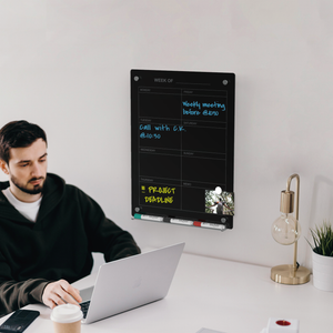 Black glass weekly planner wall mounted next to a person working for organization and planning. 